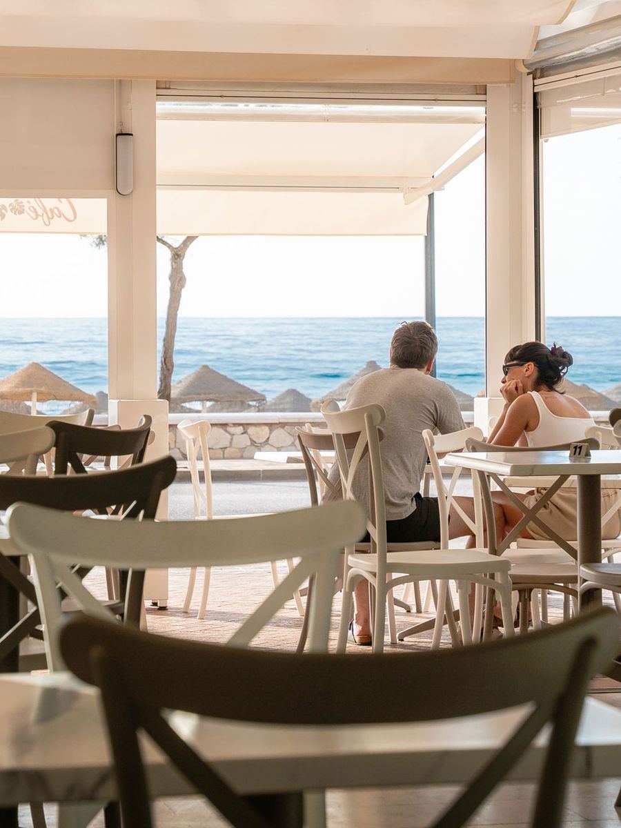 View from a table: straw parasols on the beach and the Mediterranean beyond.